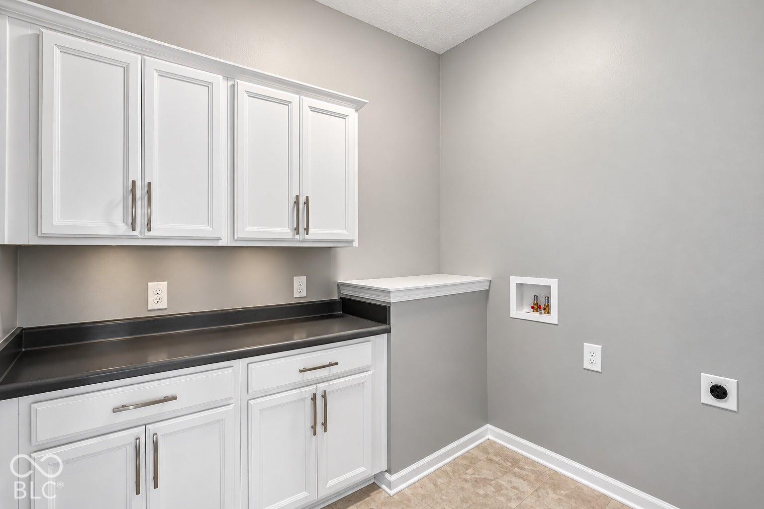 White cabinetry with brushed nickel hardware, dark gray countertops, integrated under-cabinet lighting, and tile flooring