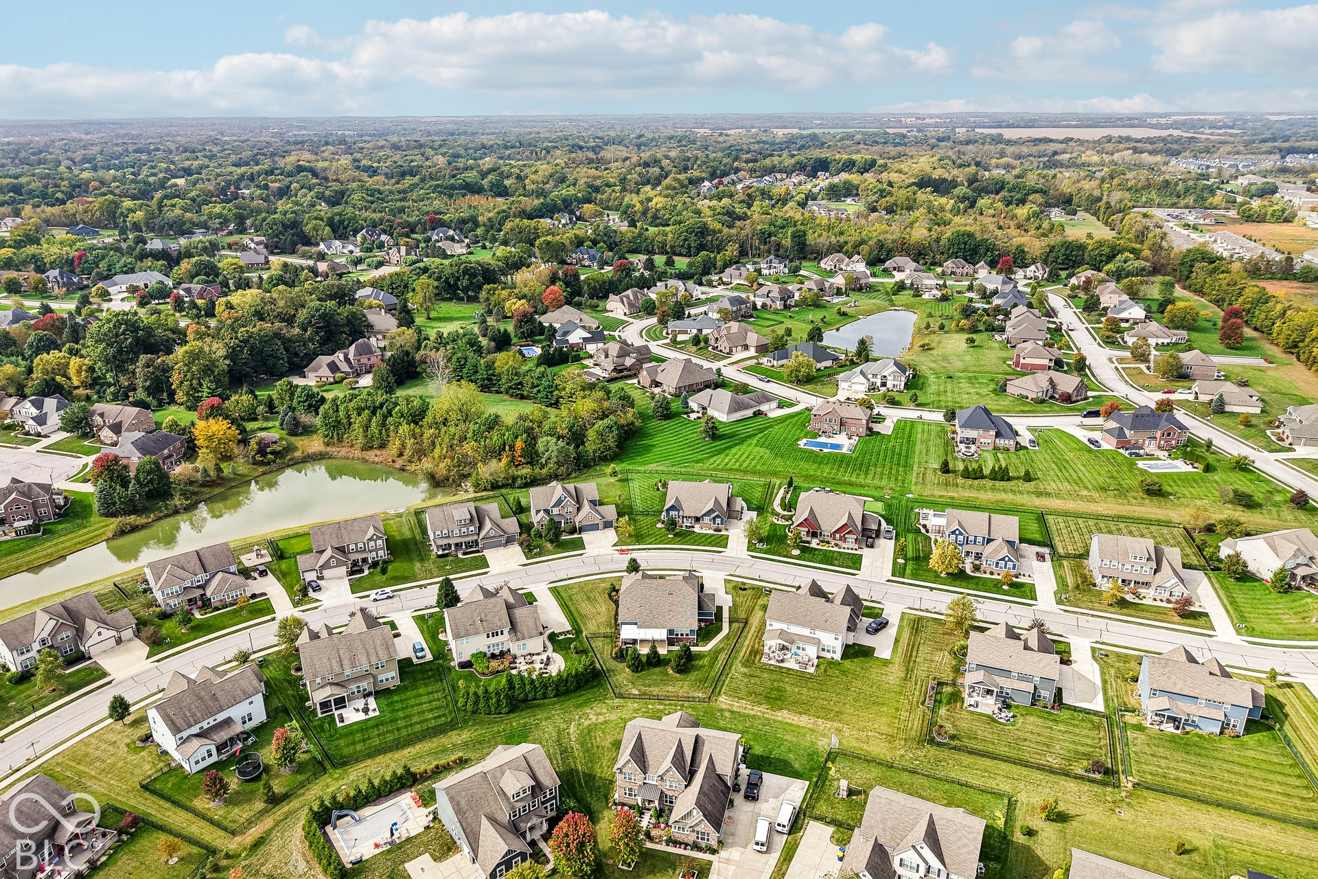 Expansive residential development with large lots, mature trees, a retention pond, and paved roadways