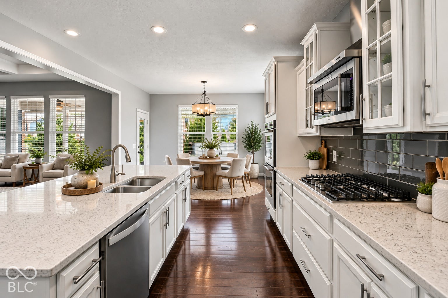 Open-concept kitchen with wood-finish flooring, white cabinetry, integrated stainless steel appliances, a double basin sink, and ample counter space