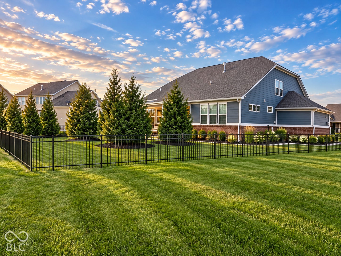 Expansive lawn area with black metal fencing and mature evergreen trees