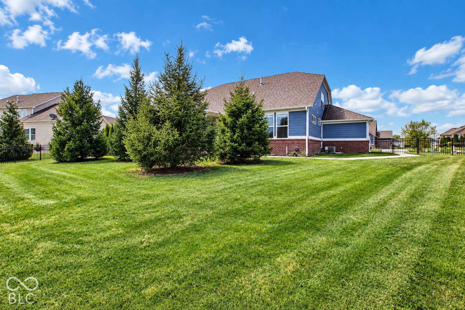 Expansive green lawn with mature evergreen trees, blue siding, and brick foundation