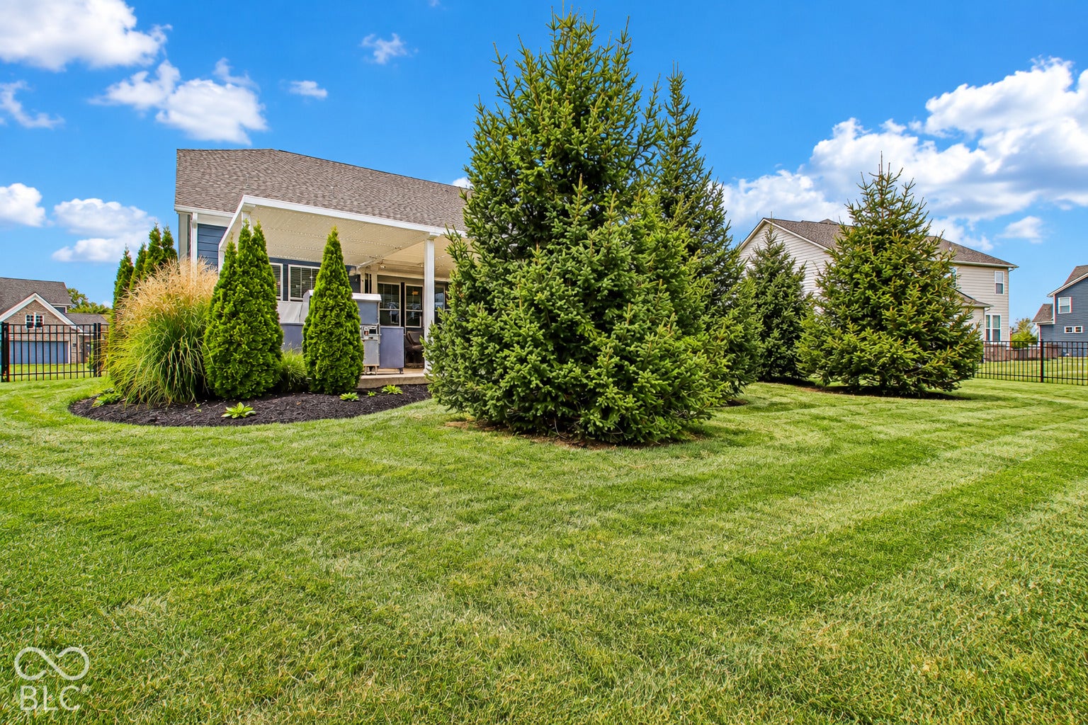 Expansive yard with lush green grass, mature evergreen trees, and manicured landscaping