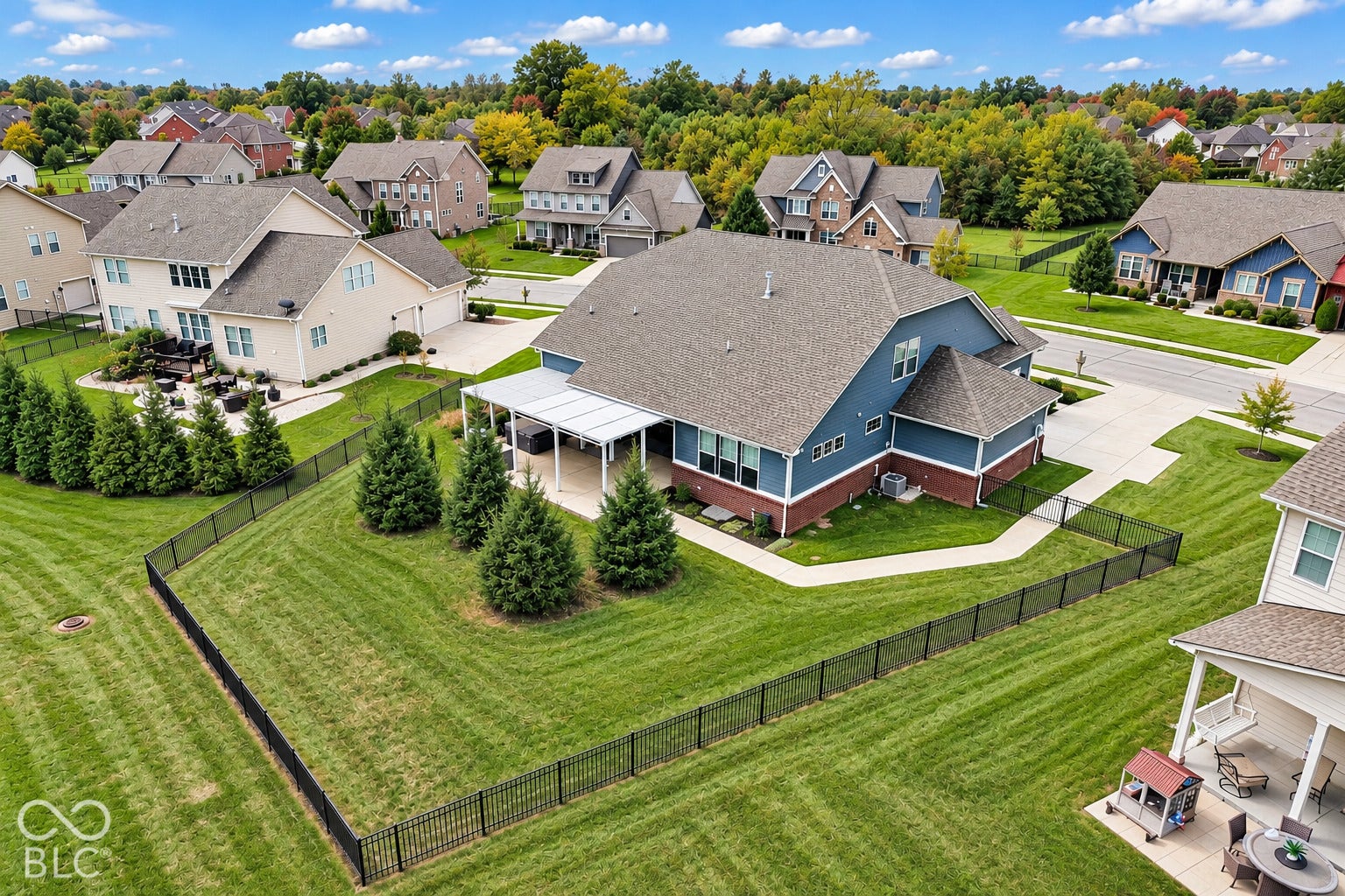Expansive fenced yard featuring a covered patio, established landscaping, and a two-story residence with a multi-gabled roof and a two-car garage