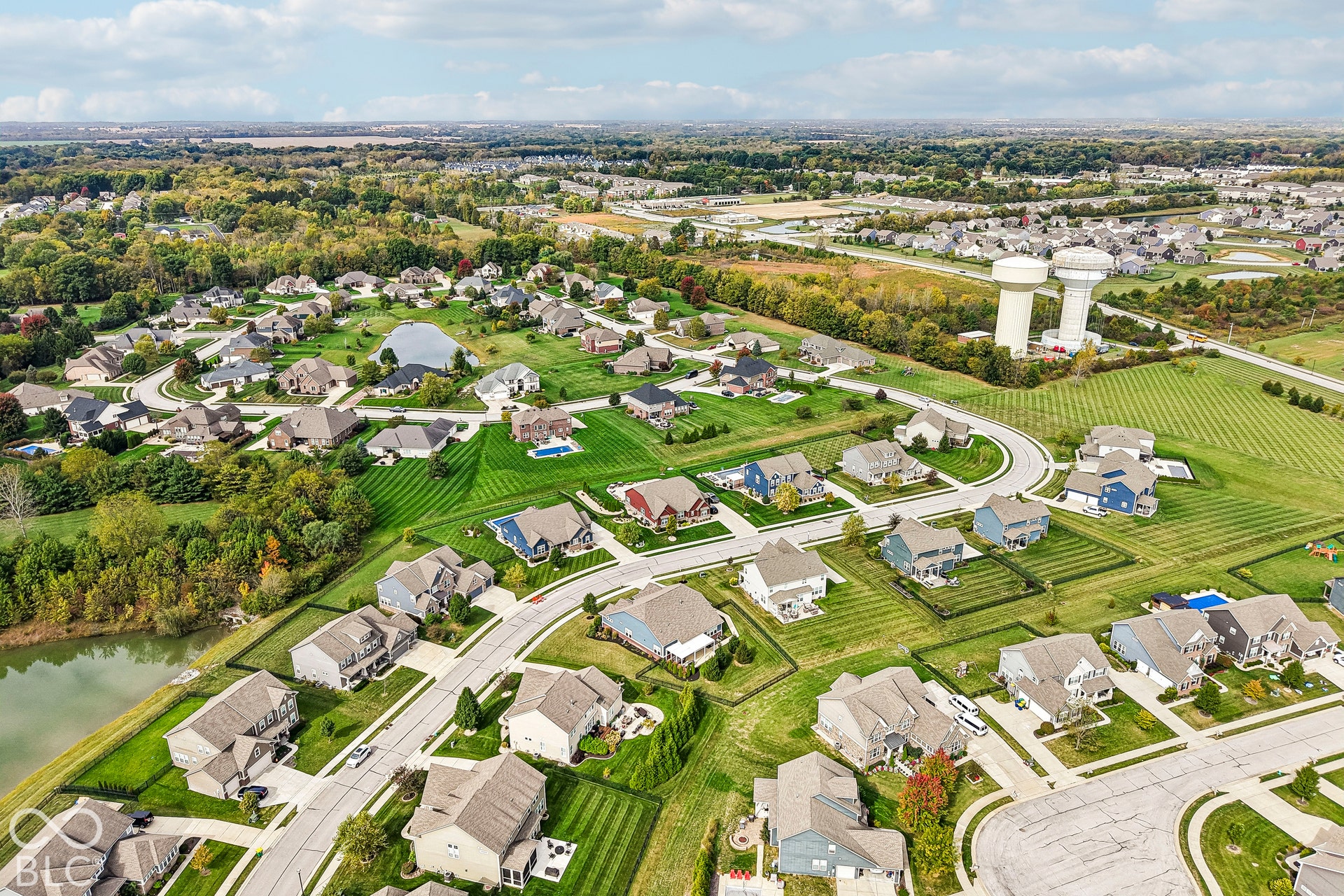 Expansive residential area featuring numerous single-family homes, mature landscaping, paved roads, and a large body of water