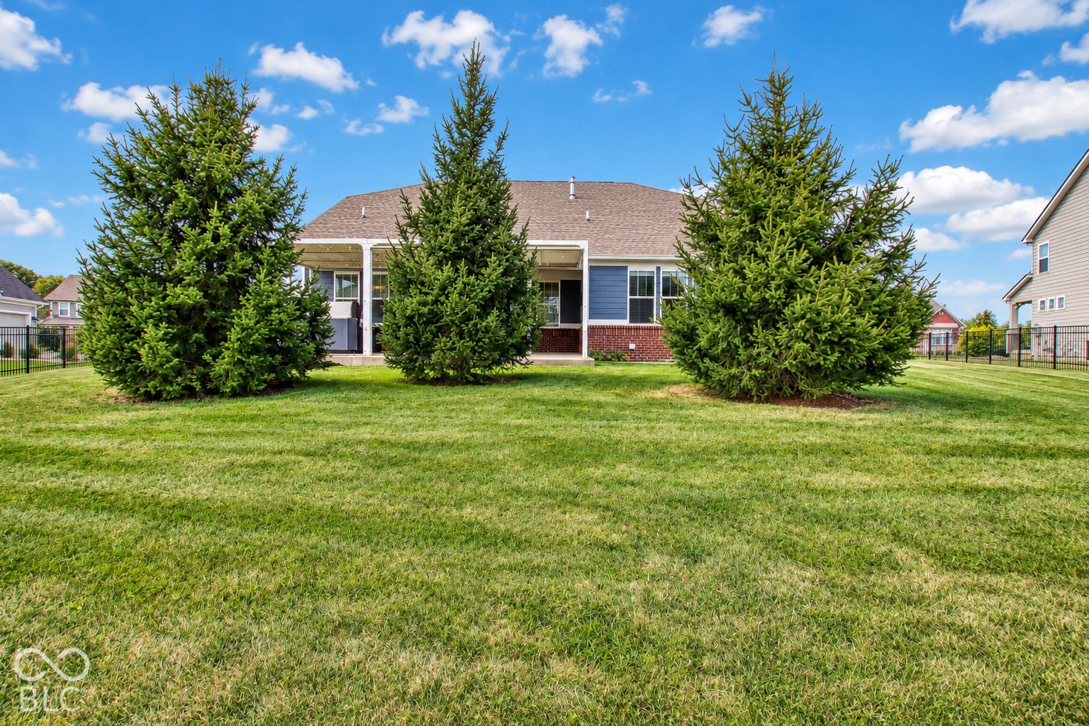 Expansive green lawn with mature evergreen trees and a covered patio