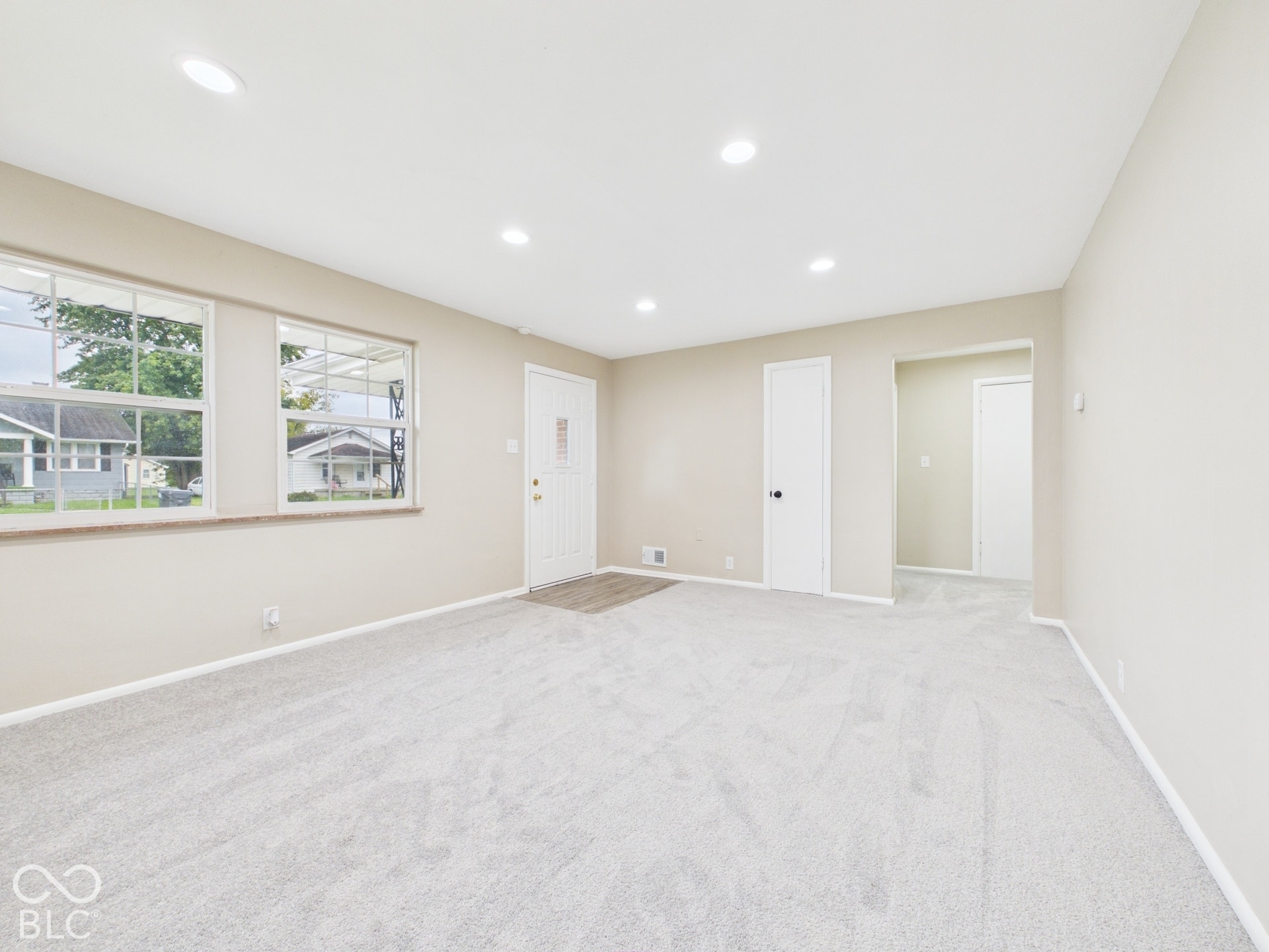 Recessed ceiling lighting, light neutral wall paint, light-colored carpet, white interior doors, and a wood-finish flooring entryway