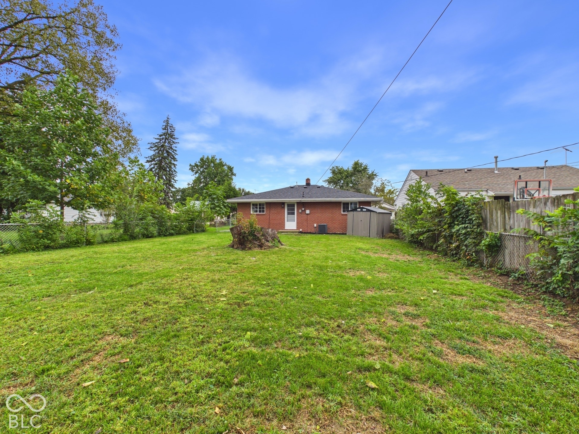 Spacious backyard featuring a large grass area, mature trees, and a chain-link fence
