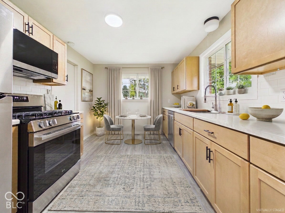 Virtually Altered - Light wood-finish cabinetry with black hardware, stainless steel appliances, white subway tile backsplash, and light-toned countertops