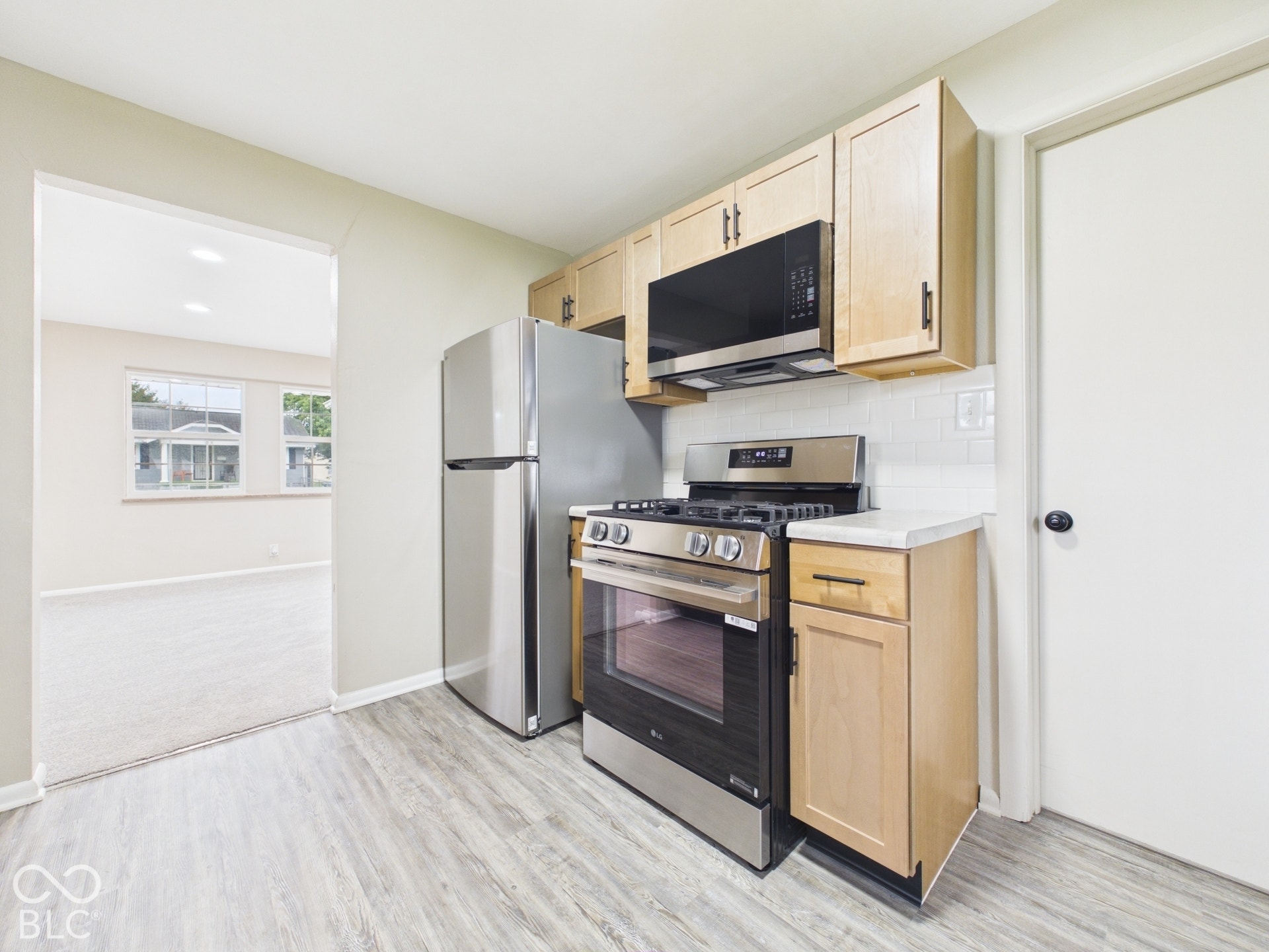 Kitchen featuring wood-finish flooring, light wood cabinetry, stainless steel appliances, white subway tile backsplash, and light countertops