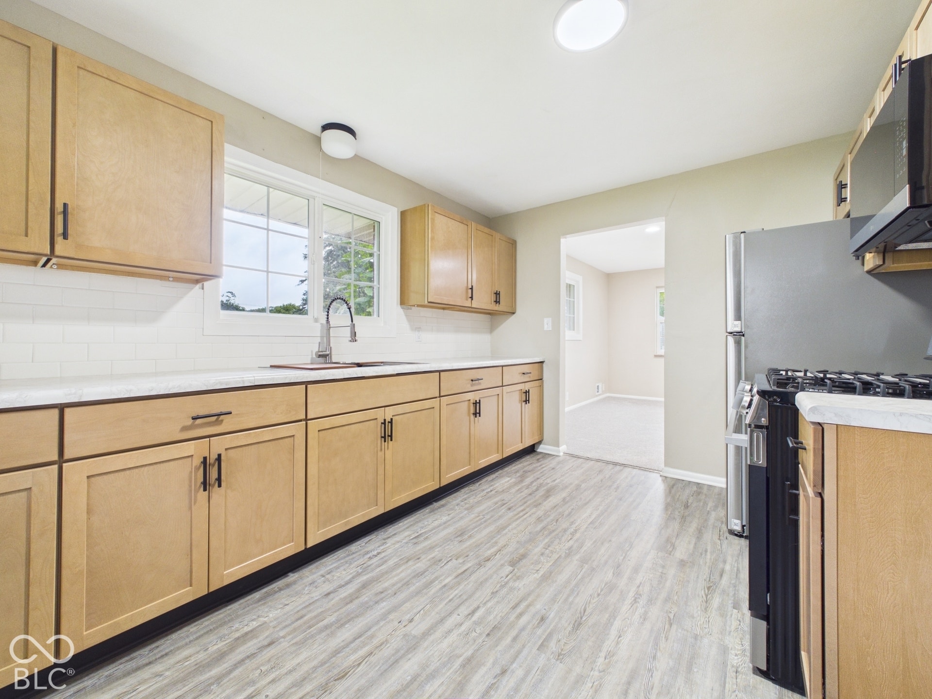 Kitchen featuring wood-finish flooring, light wood cabinetry with dark hardware, white subway tile backsplash, and a stainless steel sink with a gooseneck faucet