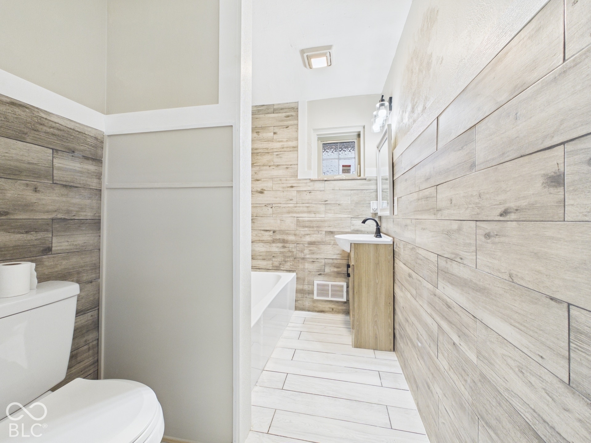 Wood-look plank wall tiling, white floor tiling, white built-in tub, and a vanity with a white basin and matte black faucet