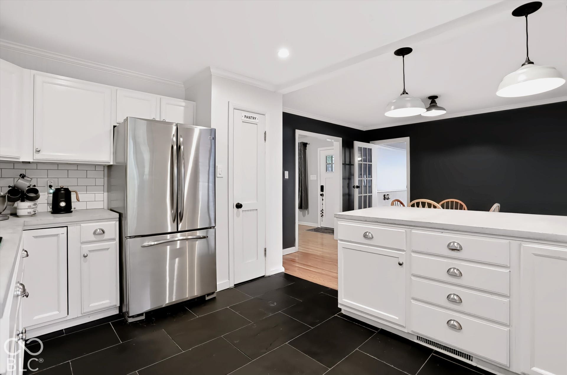 White cabinetry with brushed nickel hardware, subway tile backsplash, stainless steel refrigerator, black tile flooring, and white countertops