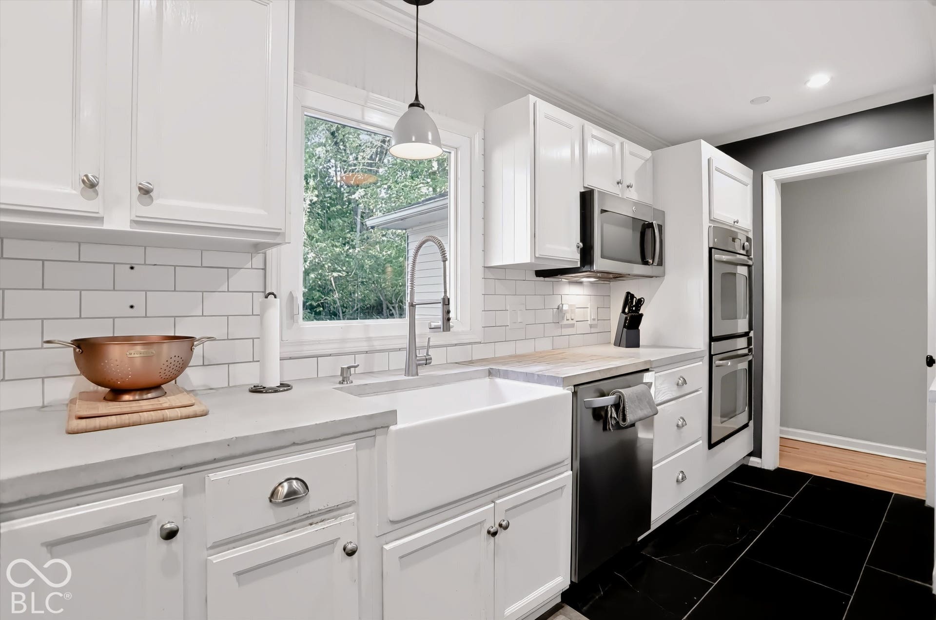 Kitchen featuring white cabinetry, subway tile backsplash, farmhouse sink, stainless steel appliances, and black tile flooring