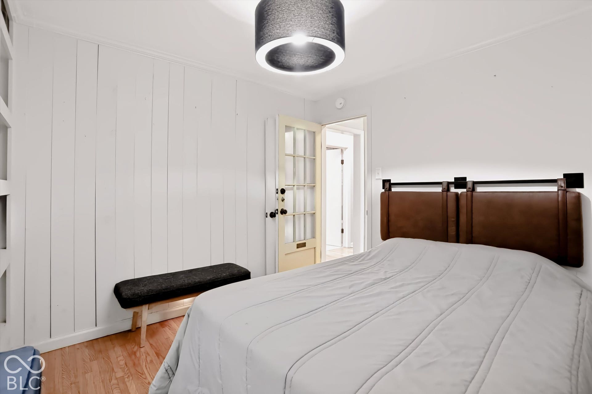 Wood-finish flooring with white vertical paneled accent wall, and a drum pendant light fixture