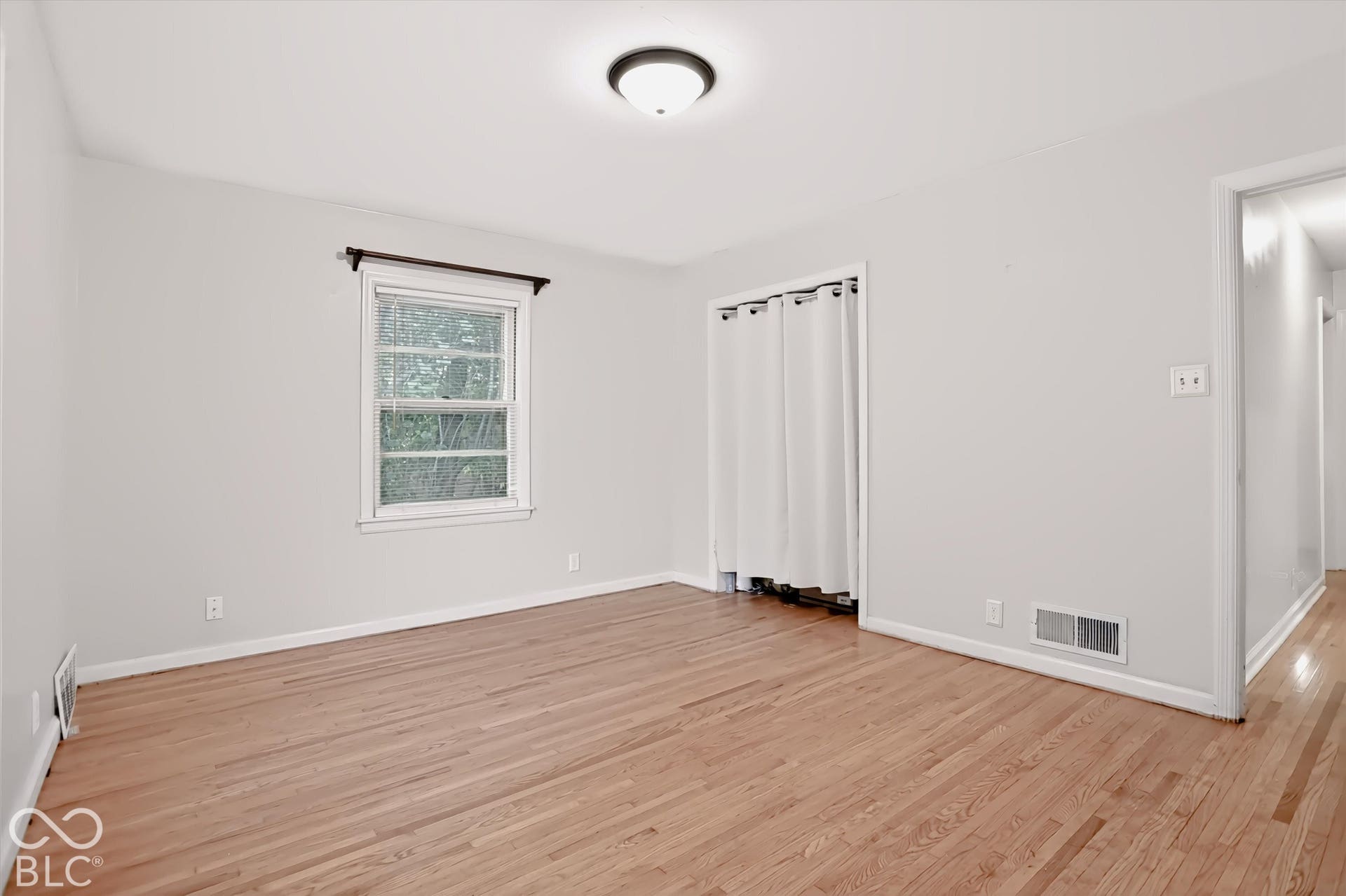Hardwood flooring, painted walls, ceiling-mounted light fixture, and a window with trim