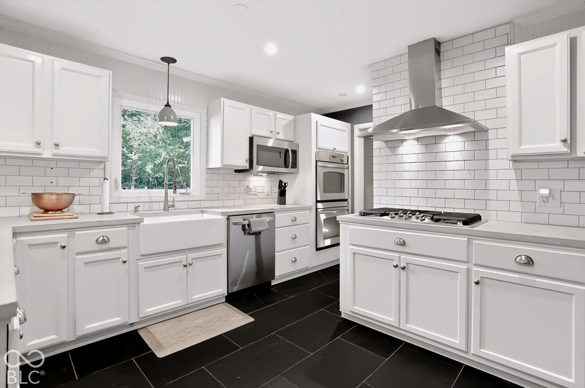 White shaker cabinetry with contrasting dark tile flooring, stainless steel appliances, a farmhouse-style sink, and subway tile backsplash