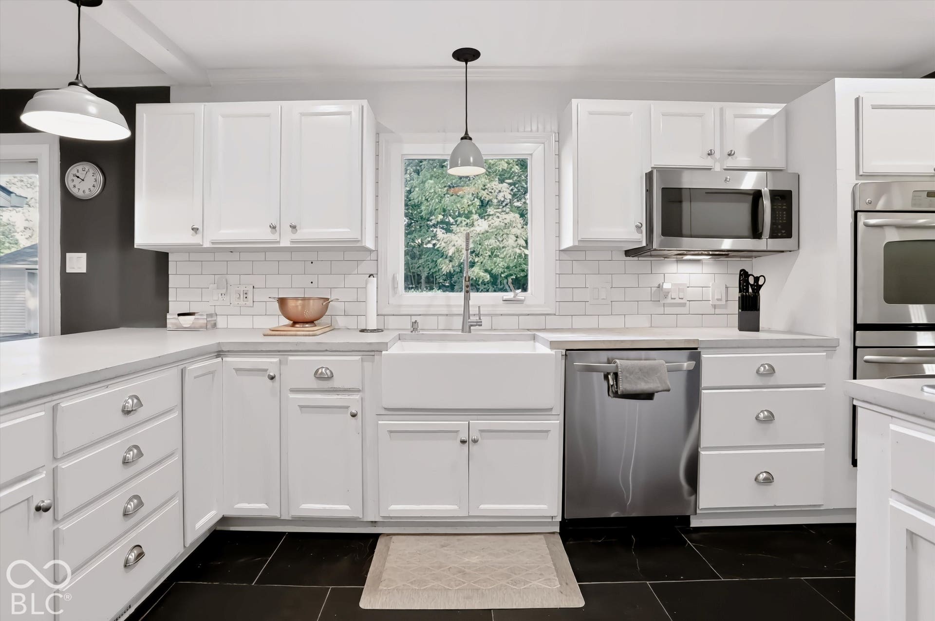 White cabinetry, white subway tile backsplash, farmhouse-style sink, stainless steel appliances, and dark tile flooring