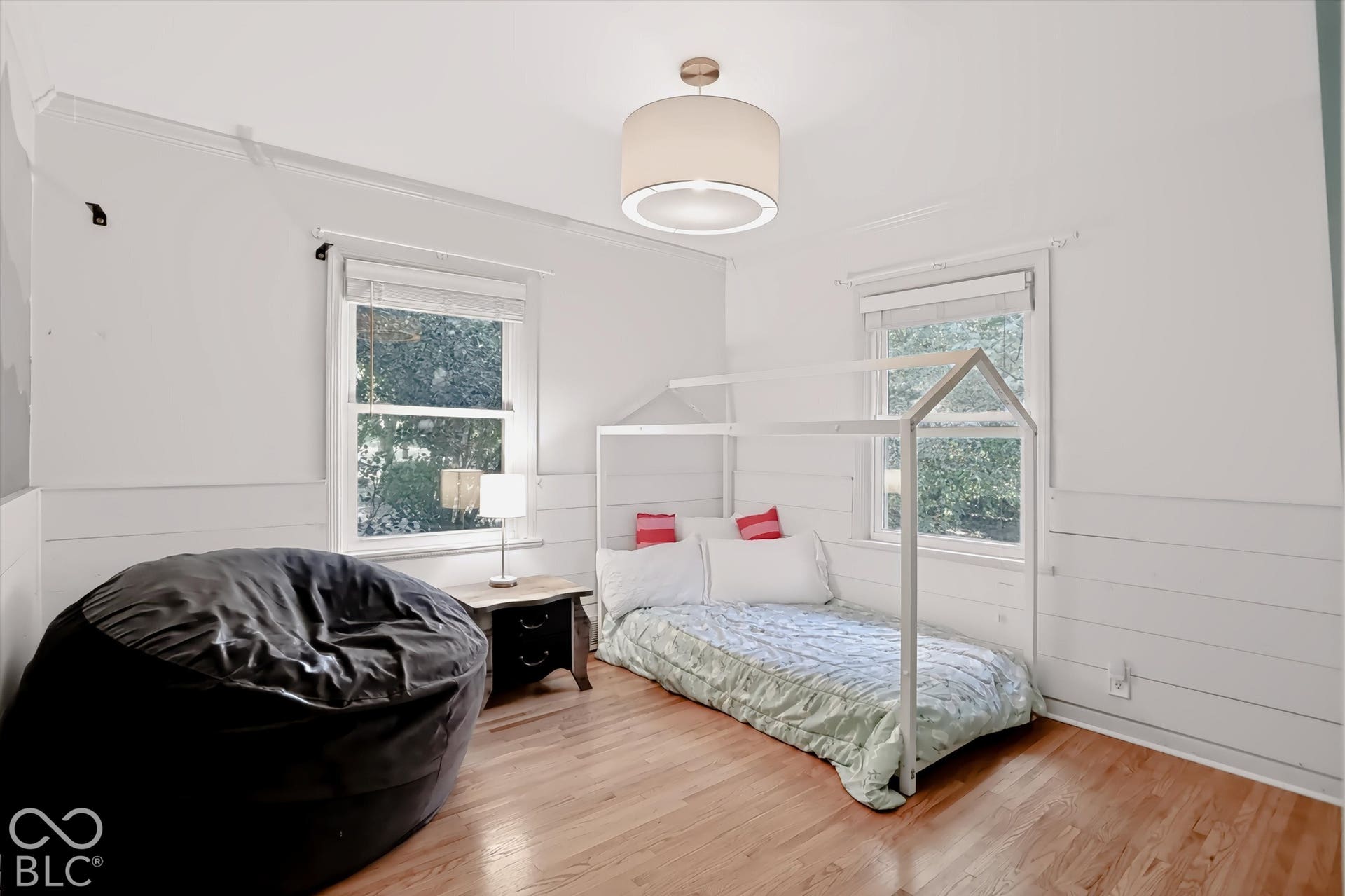 Hardwood flooring, painted shiplap accent wall, two large windows, white walls, and a drum pendant light fixture