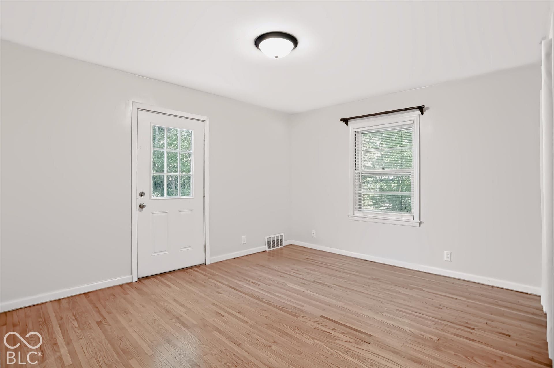 Hardwood flooring, neutral wall tones, transom window door, white trim, and a flush mount ceiling light