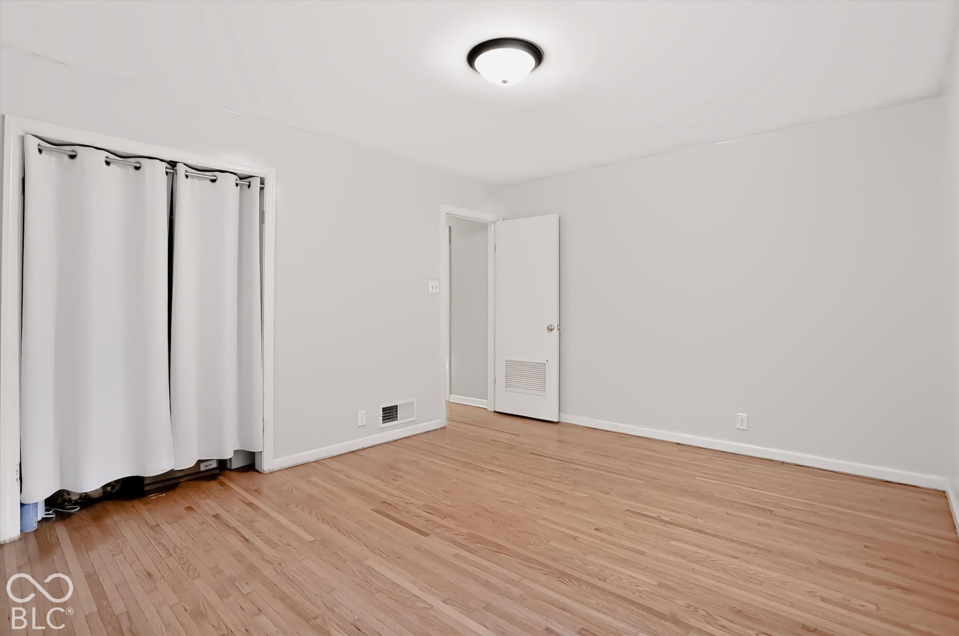 Hardwood flooring, light gray wall paint, white trim, overhead lighting, and an interior door with a silver knob