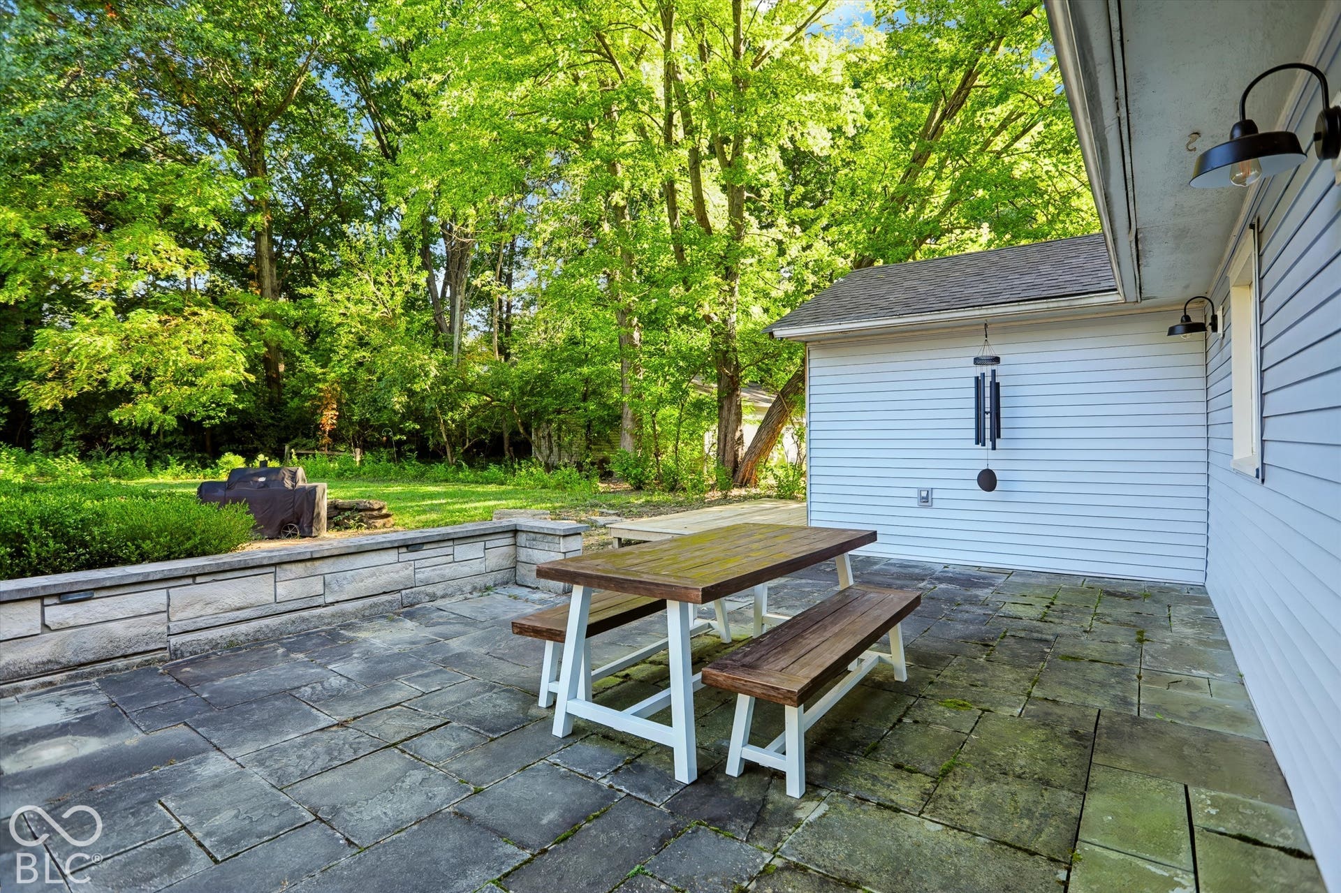 Paver patio with a stone retaining wall and an expansive grassy area surrounded by mature trees