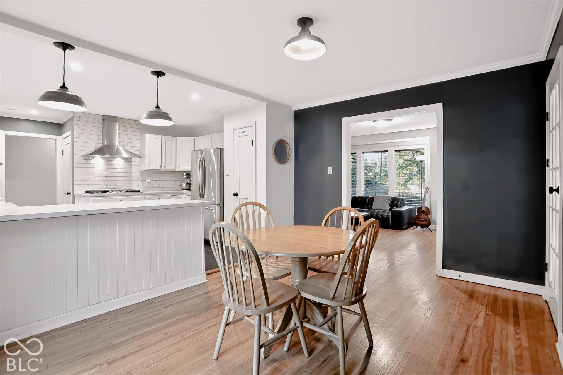 Kitchen featuring a white subway tile backsplash, stainless steel range hood, pendant lighting, and a breakfast bar with beadboard paneling