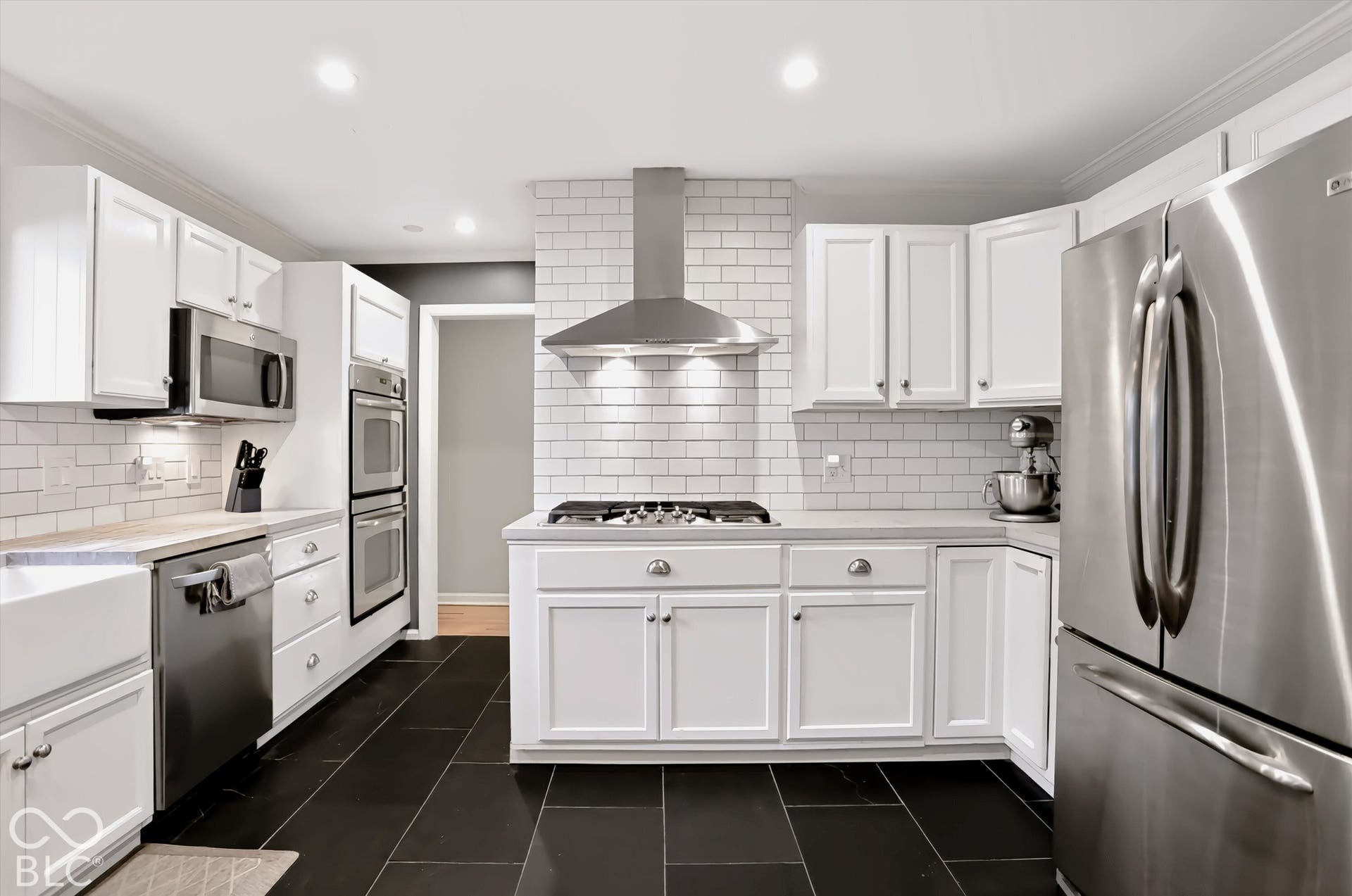 White cabinetry with stainless steel appliances, subway tile backsplash, farmhouse sink, and recessed lighting