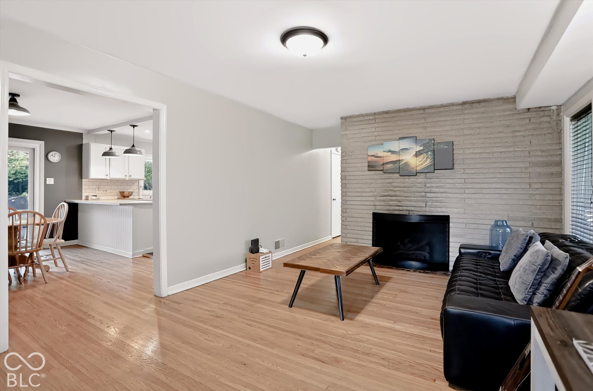 Hardwood-finish flooring, a stone-faced fireplace with a dark insert, a kitchen pass-through with pendant lighting, and recessed ceiling lighting