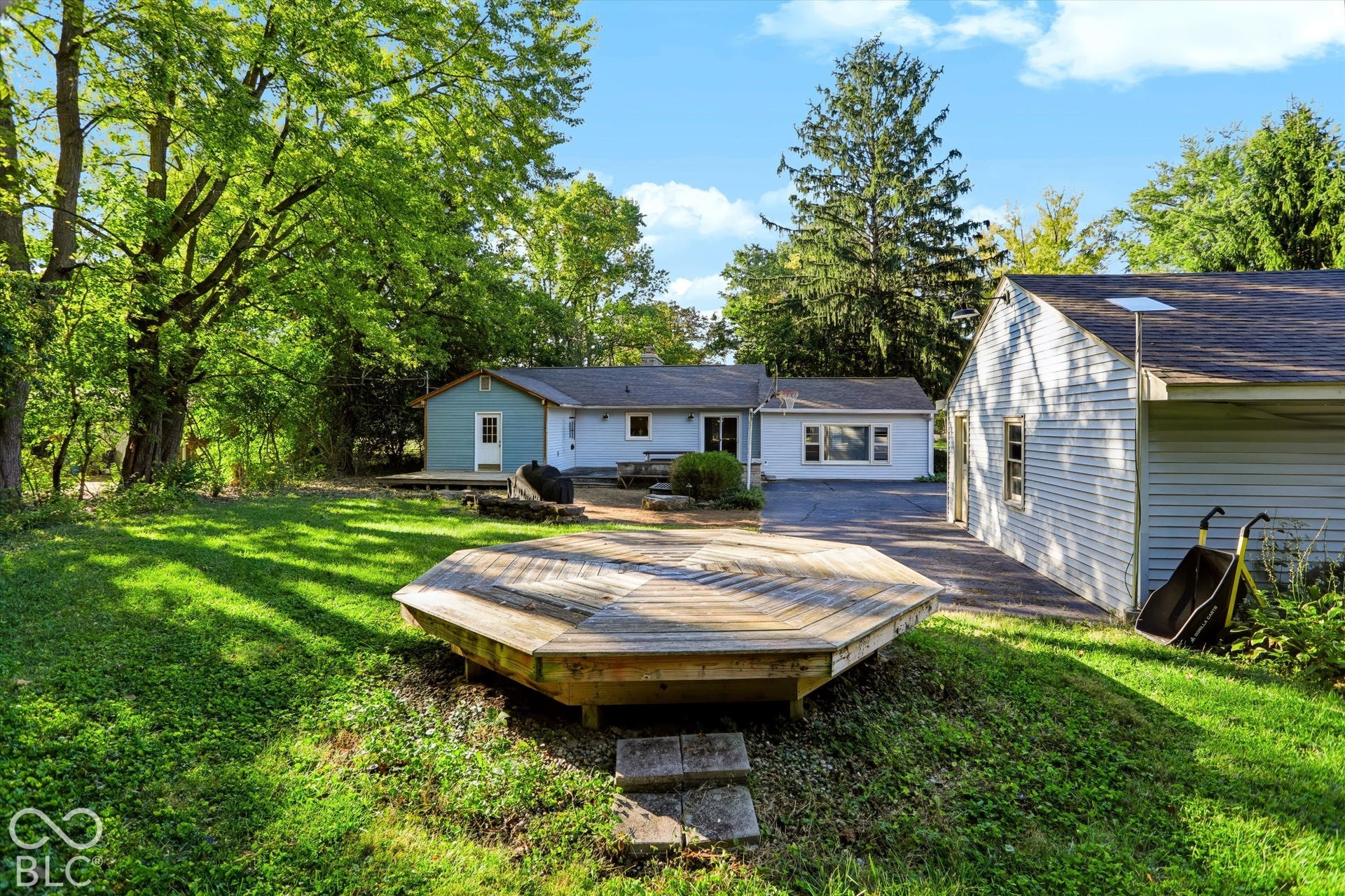 Expansive yard featuring a wooden deck, concrete patio, and mature trees