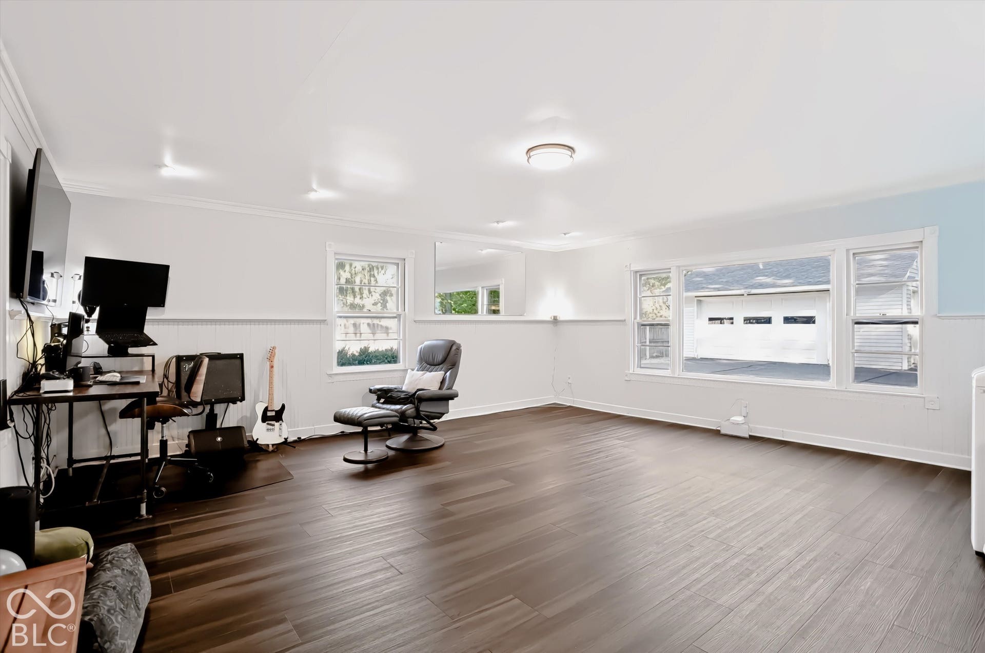 Dark wood-finish flooring, white paneled walls, multiple windows, and recessed lighting