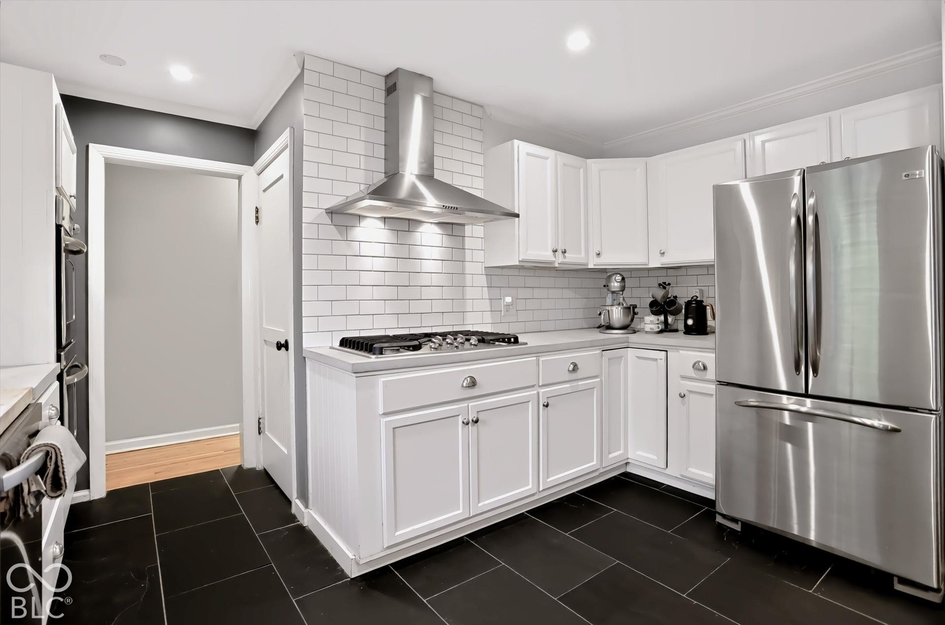 Kitchen featuring stainless steel appliances, white cabinetry, a gas range with a stainless steel range hood, subway tile backsplash, and dark tile flooring