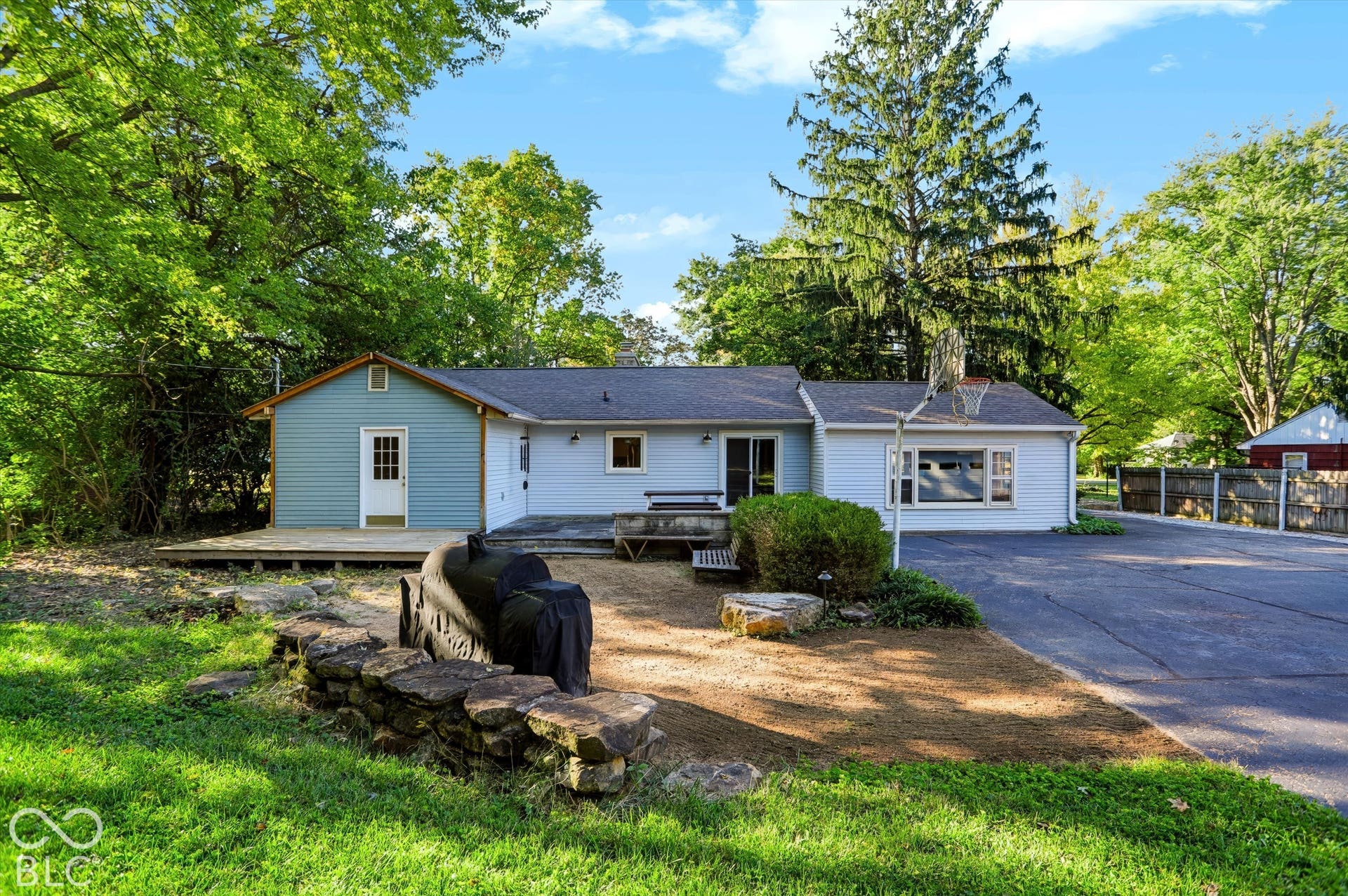 Exterior featuring light blue siding, a dark asphalt shingle roof, a rear wood deck, and a paved driveway