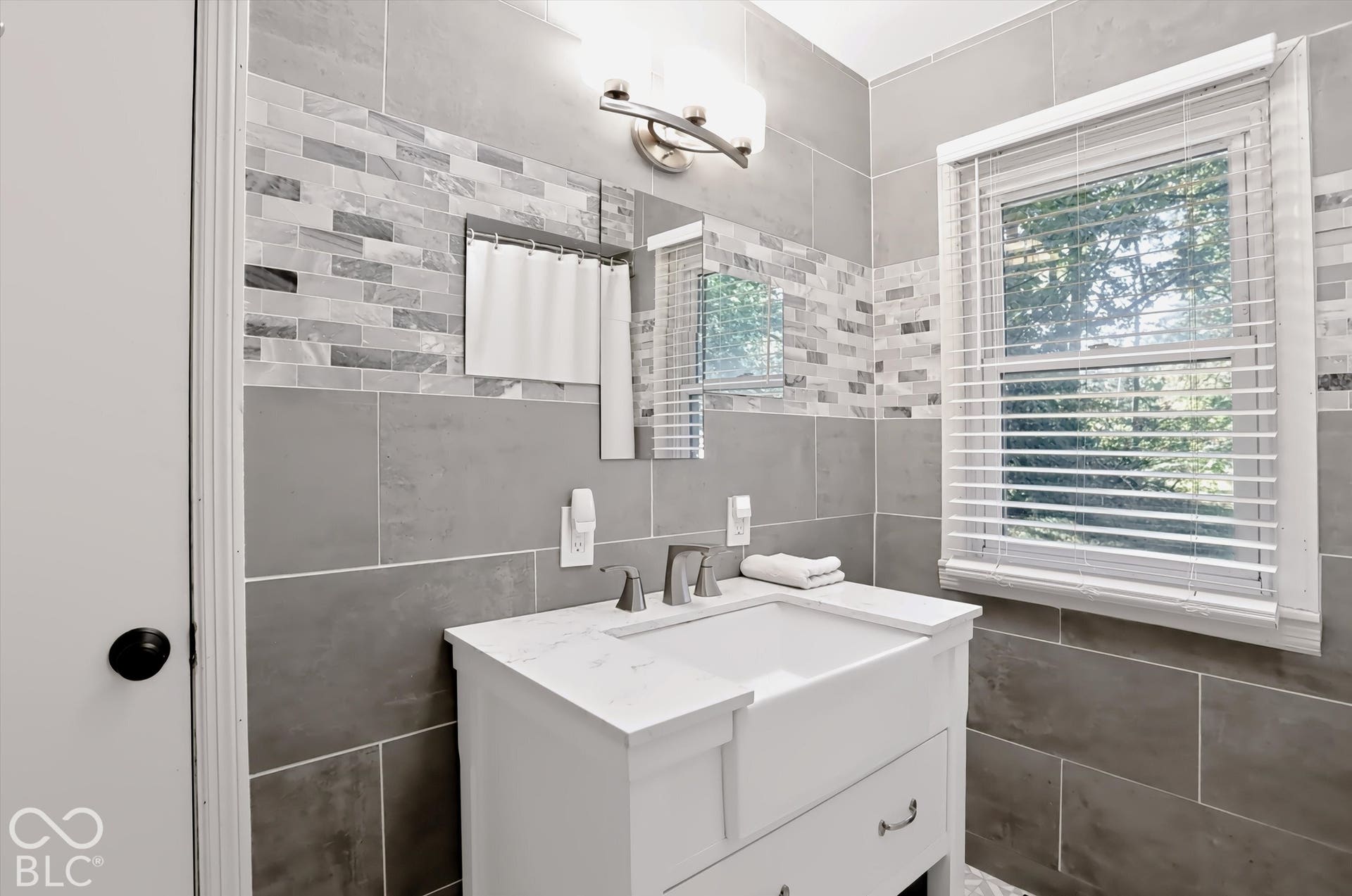 Vanity with an integrated rectangular sink, wall-mounted light fixture, and a tiled accent wall