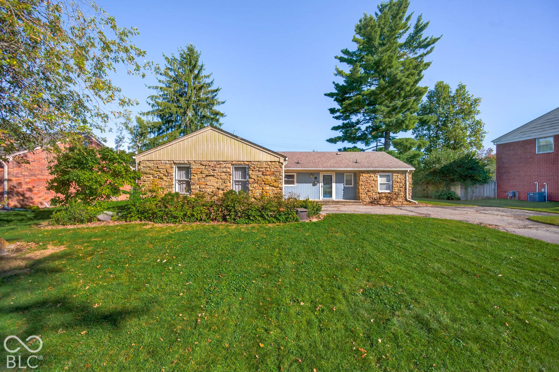 Stone exterior with partial siding, mature trees, and a front lawn