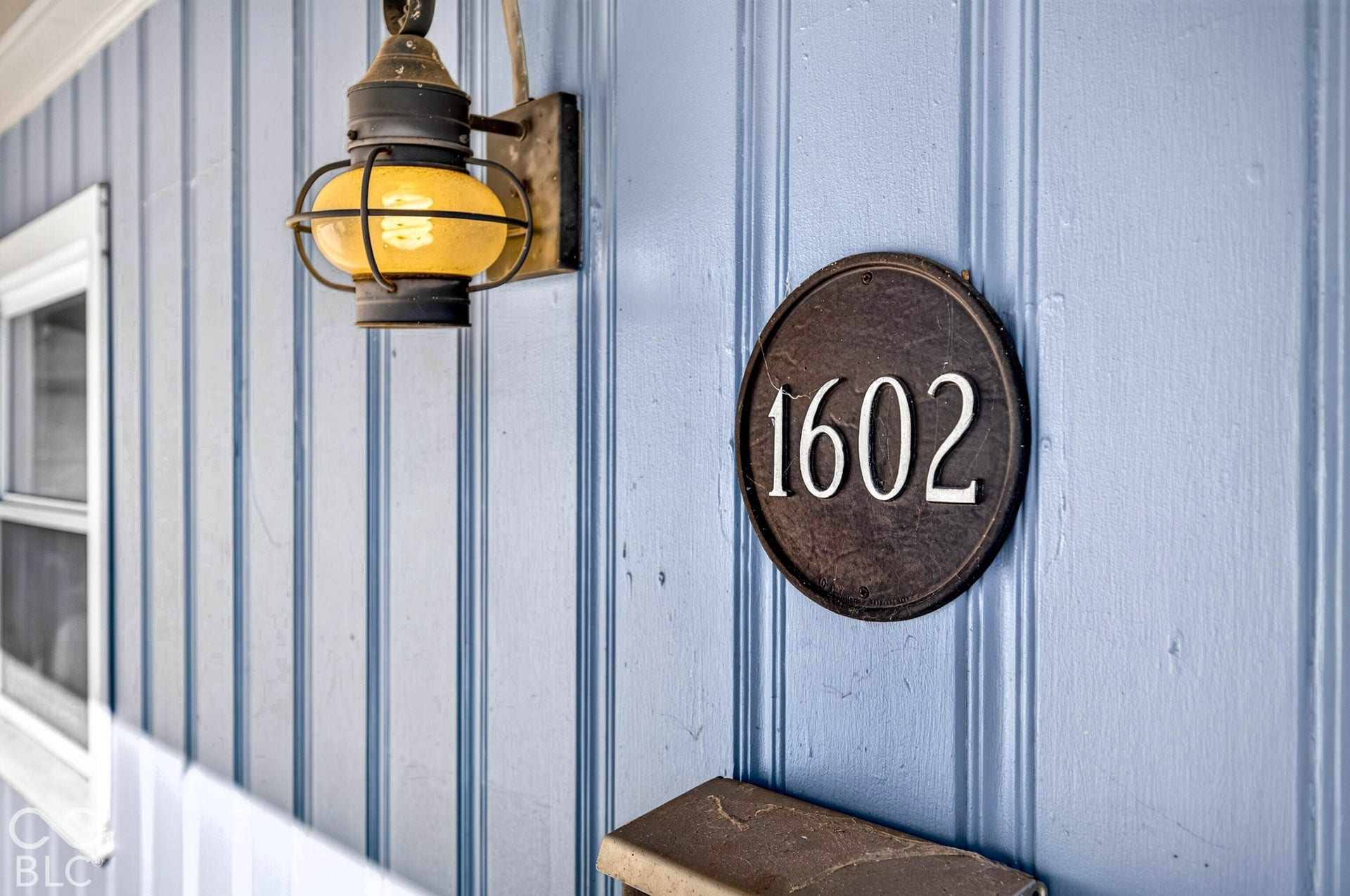 Board-and-batten siding with a wall-mounted lantern and a circular address plaque