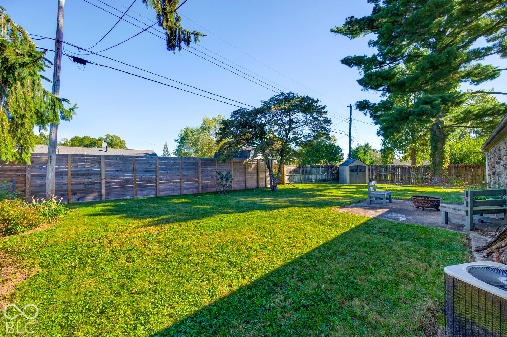 Expansive grassy yard with a privacy fence, mature trees, and a storage shed