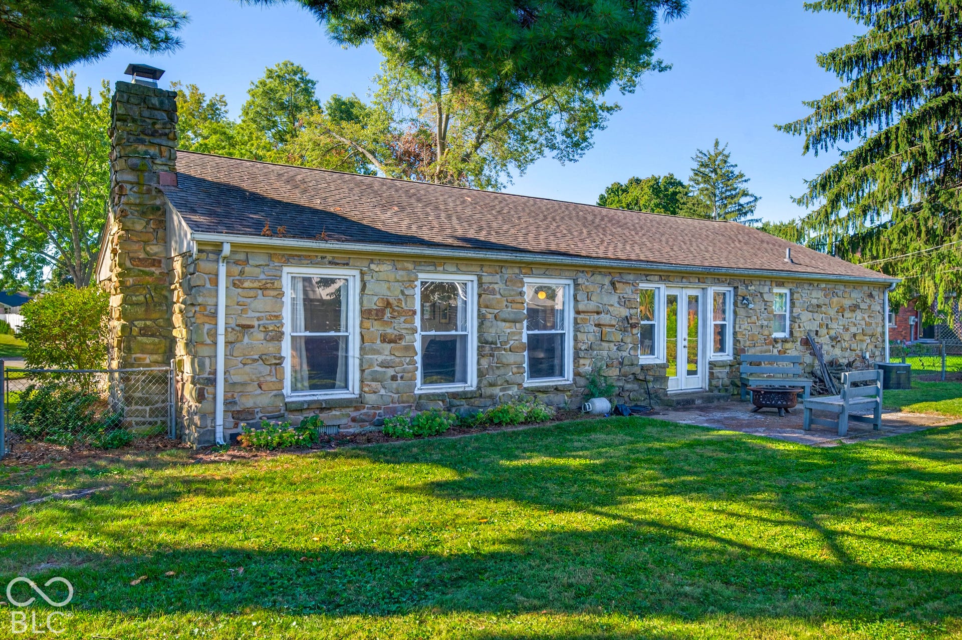 Stone exterior with a prominent stone chimney, multiple windows, double doors, and an exterior patio