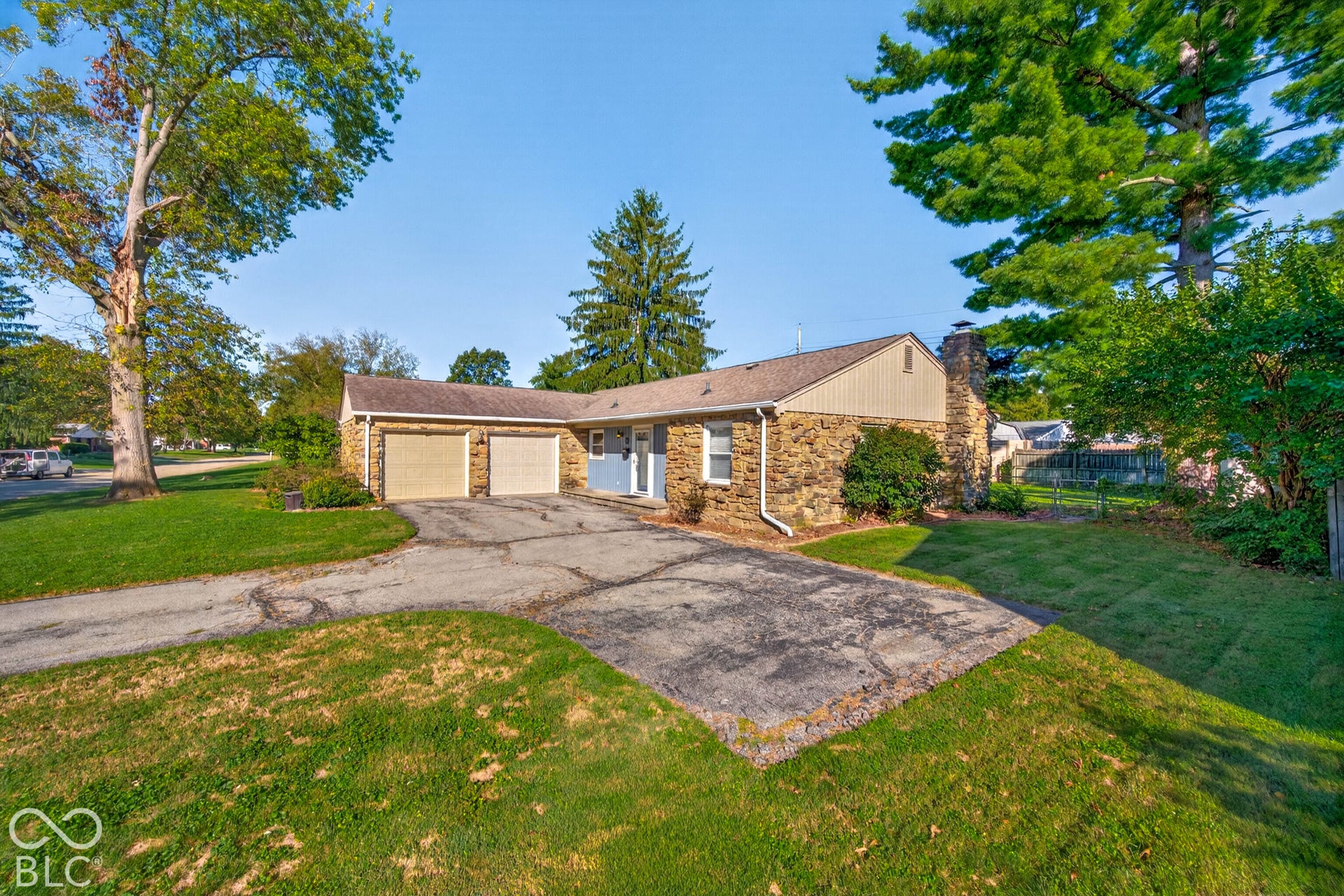 Stone exterior featuring a light blue entry door, an attached two-car garage, and mature trees