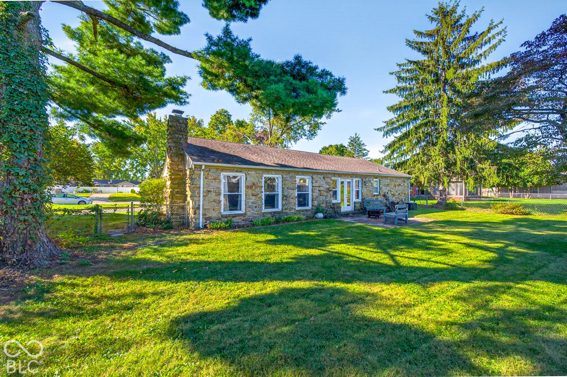 Stone exterior residence featuring a prominent stone chimney, multiple windows, and a paved patio area