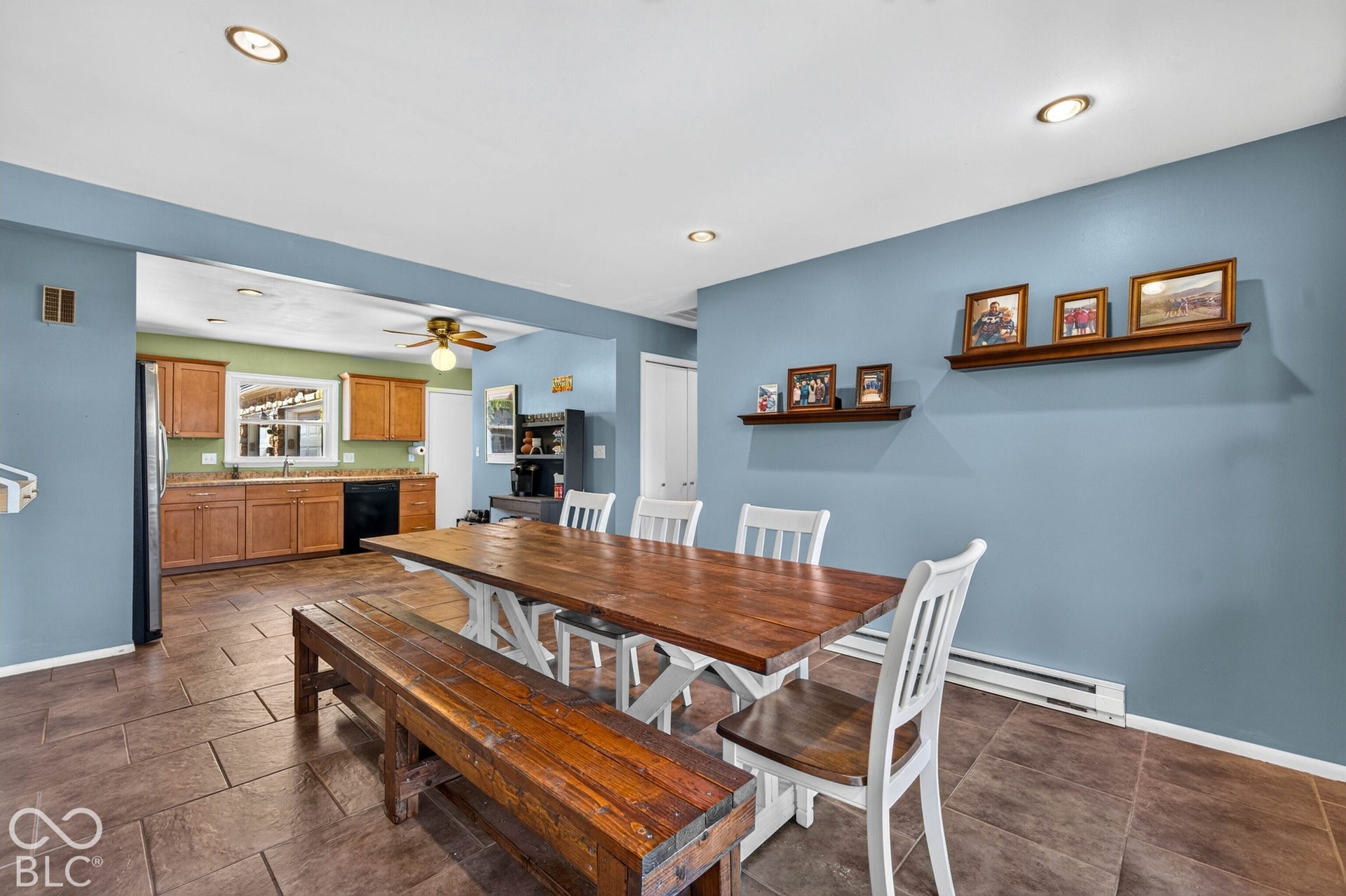 Dining area showcasing a wood-finish table with matching bench seating and white ladder-back chairs, complemented by recessed ceiling lighting and soft blue wall finishes