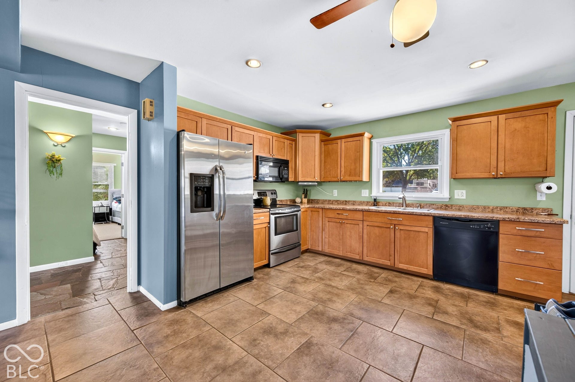 Kitchen featuring stainless steel appliances, wood cabinetry, tile flooring, and a ceiling fan with integrated lighting