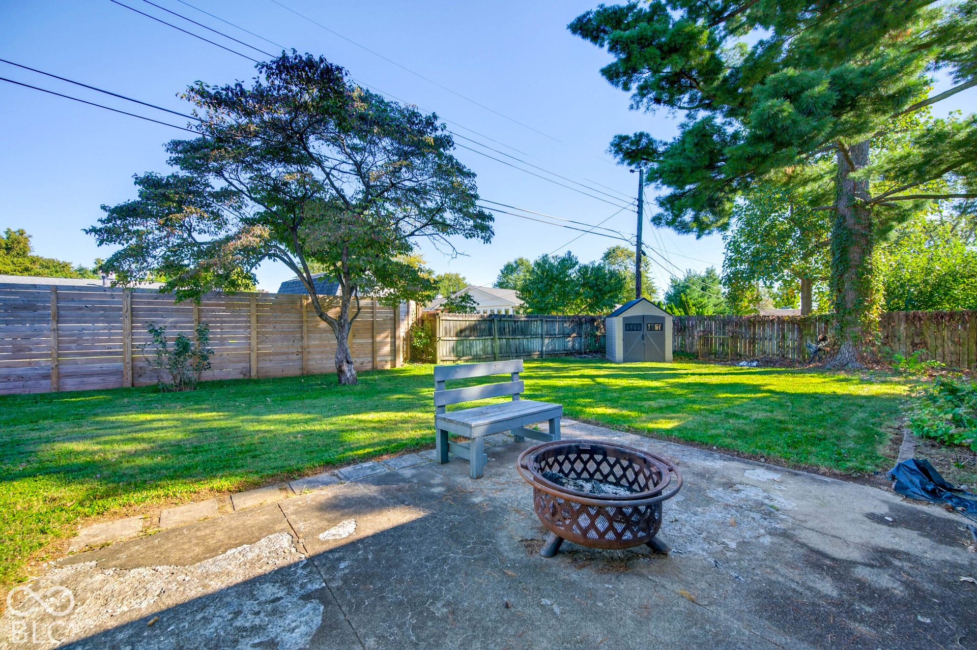 Expansive backyard featuring a concrete patio, mature trees, wood privacy fencing, and a storage shed