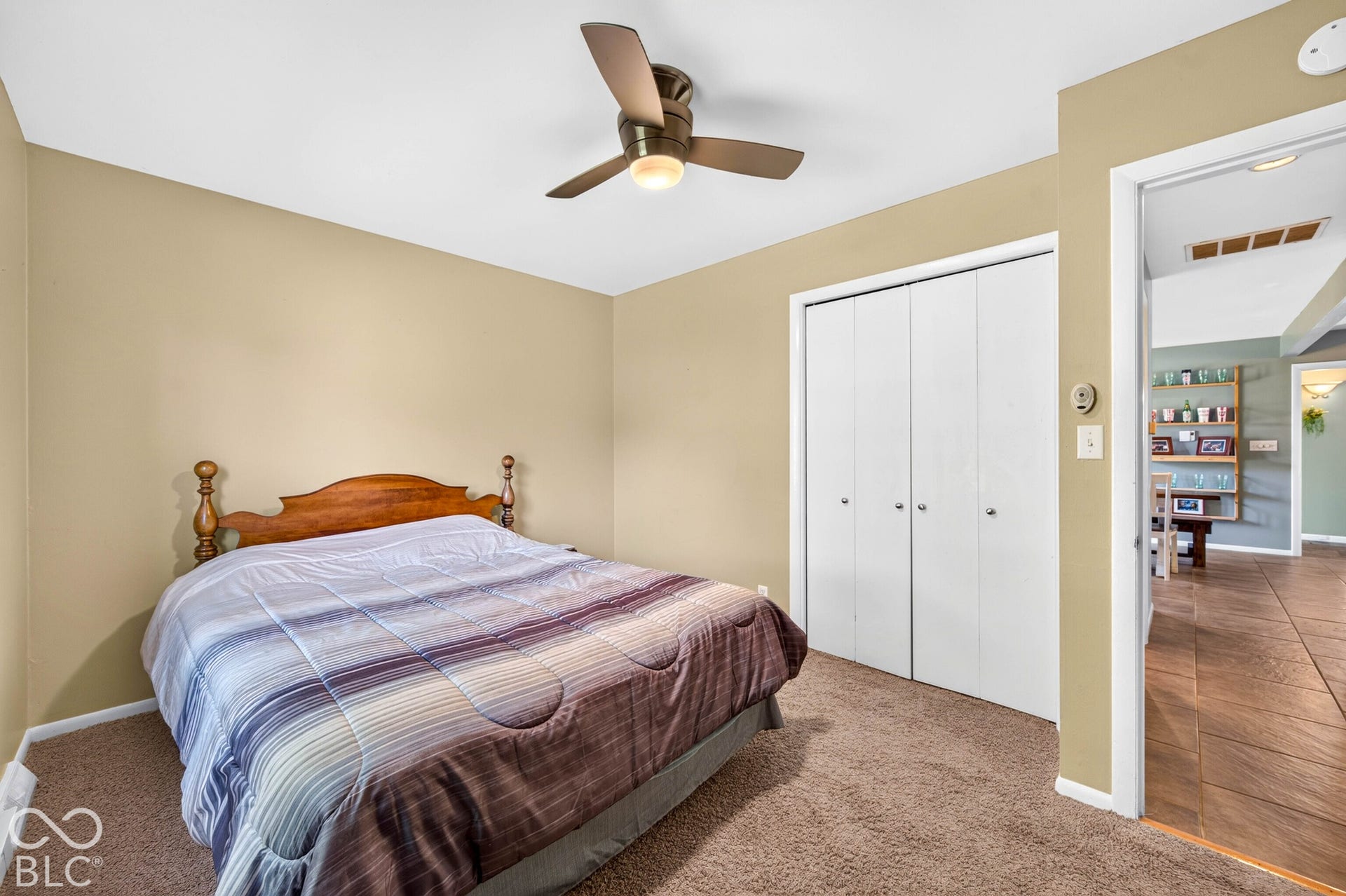 Neutral tone wall paint, textured carpeting, ceiling fan with integrated lighting, and bi-fold closet doors