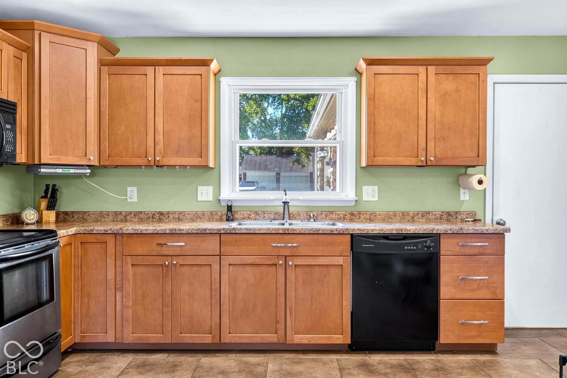 Wood-finish cabinetry with silver-tone hardware, a black built-in microwave, and a black built-in dishwasher
