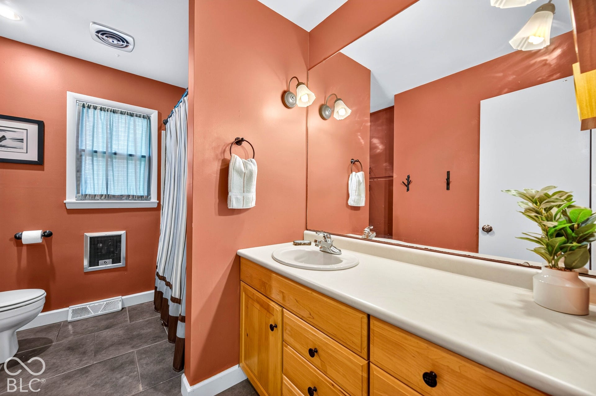 Spa-inspired primary bathroom featuring warm terracotta walls, a wood-finish vanity with dual storage, white quartz countertop, and polished chrome fixtures