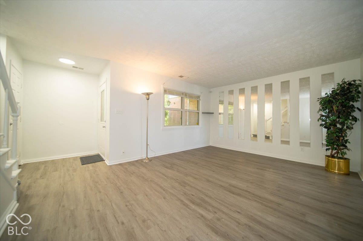 Wood-finish flooring throughout, white painted walls, window with horizontal blinds, and a staircase with white balusters