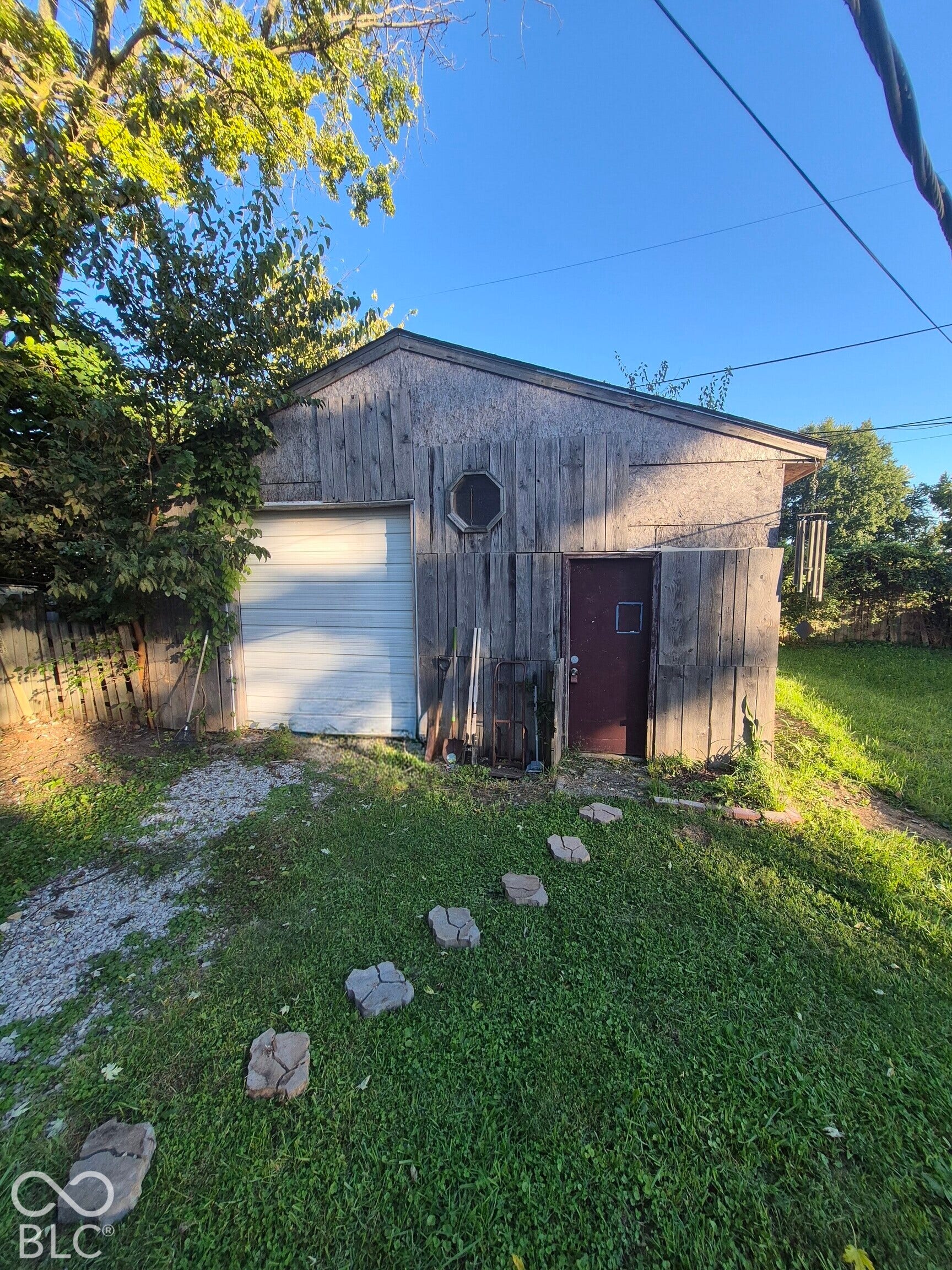 Detached structure featuring a garage door, side entry door, octagonal window, wood siding, and gabled roof