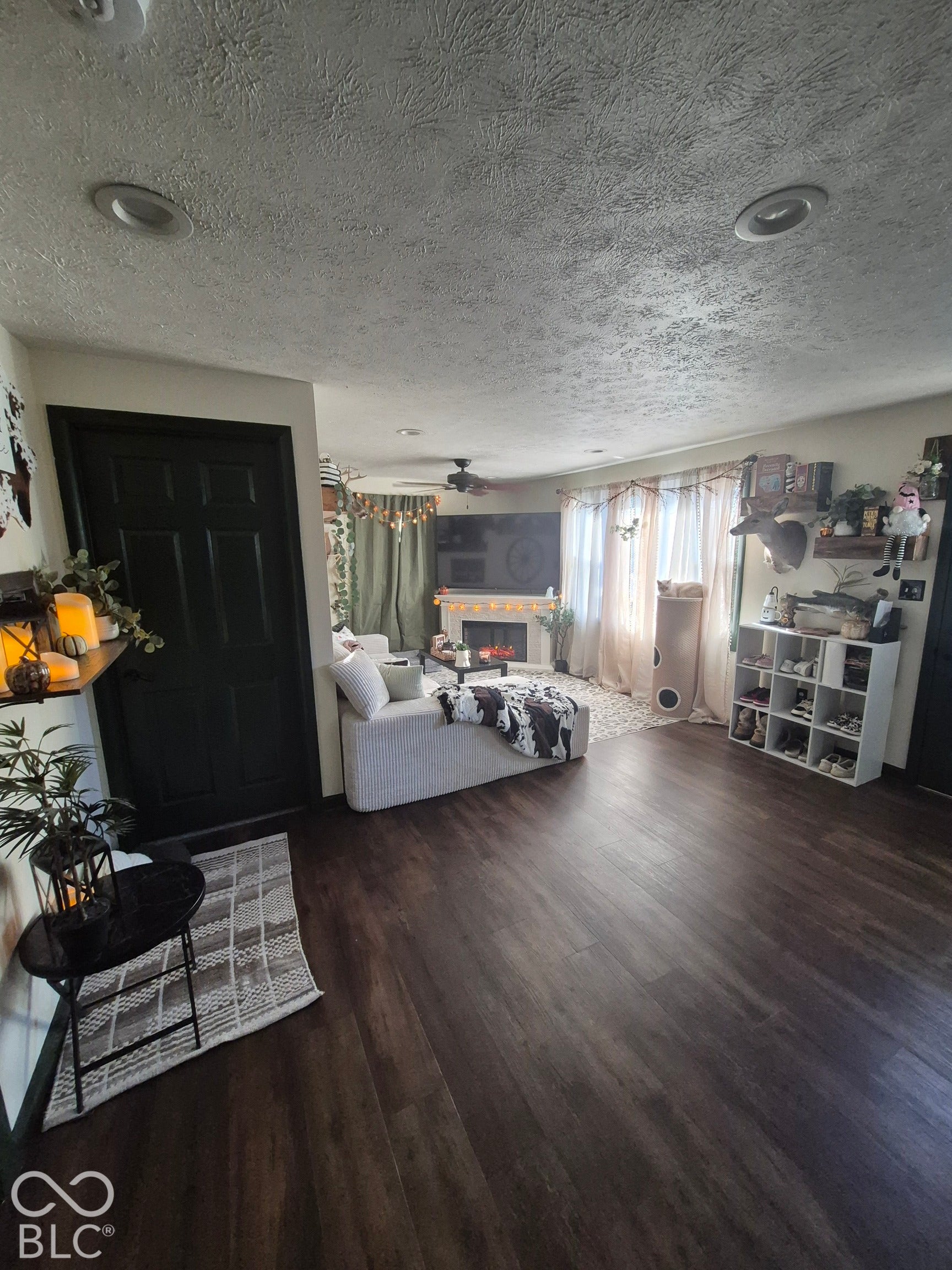 Wood-finish flooring throughout, recessed ceiling lighting, a ceiling fan with integrated lighting, and a white fireplace surround