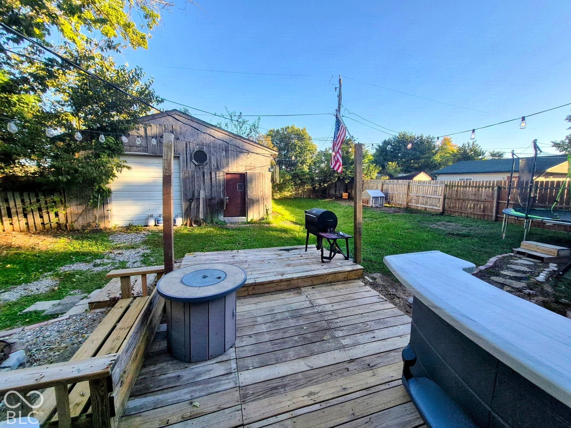 Expansive backyard featuring a wood deck, built-in bar, and a detached wooden outbuilding with a garage door and side entry