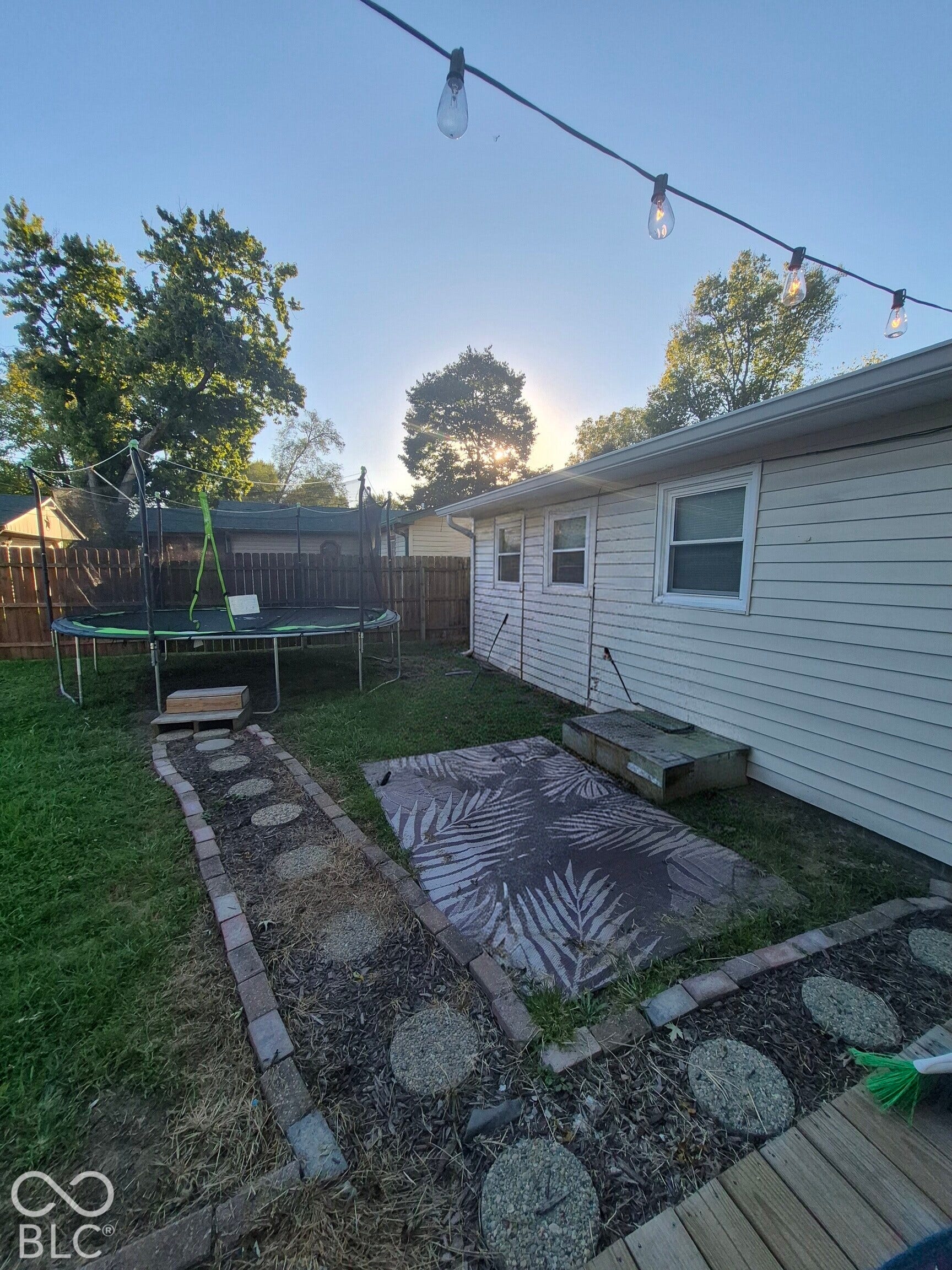 Exterior siding with multiple windows, string lighting, and a fenced perimeter